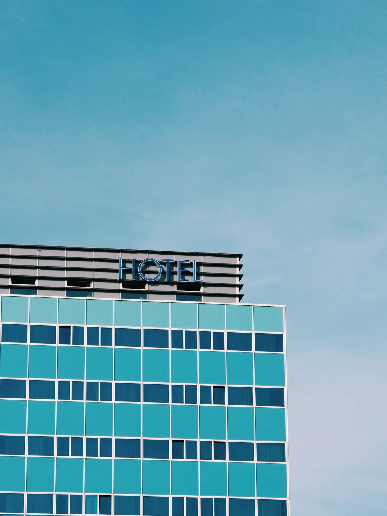 Modern teal hotel building with a HOTEL sign against a blue sky